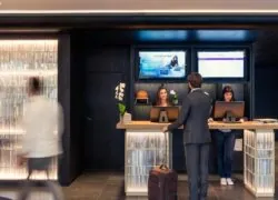 hotel reception area with guests arriving and staff behind the front desk, digital information screens visible in the background