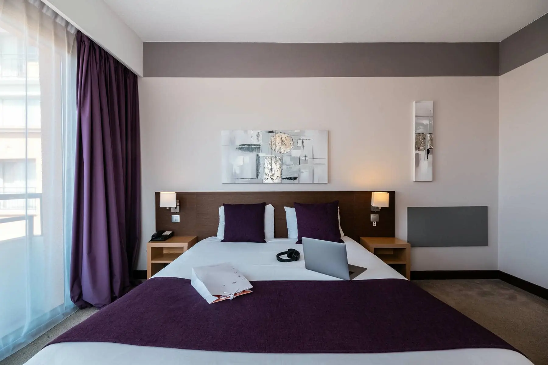 une chambre d'hôtel avec des rideaux violets et un ordinateur portable sur le lit