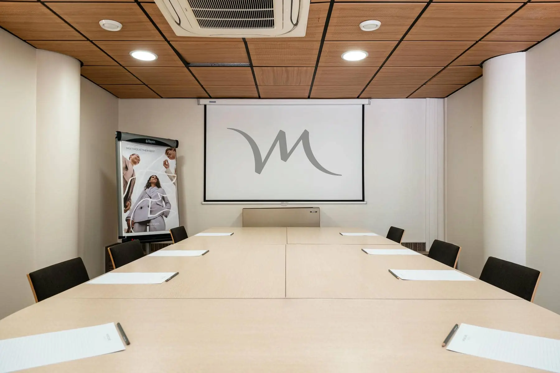 une salle de conférence avec un écran de projection sur lequel figure la lettre m