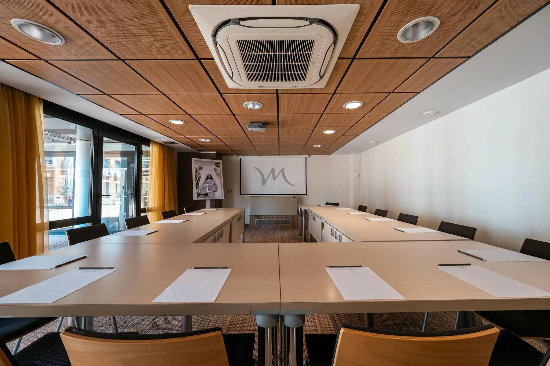 une salle de conférence avec un écran de projection sur lequel figure la lettre m