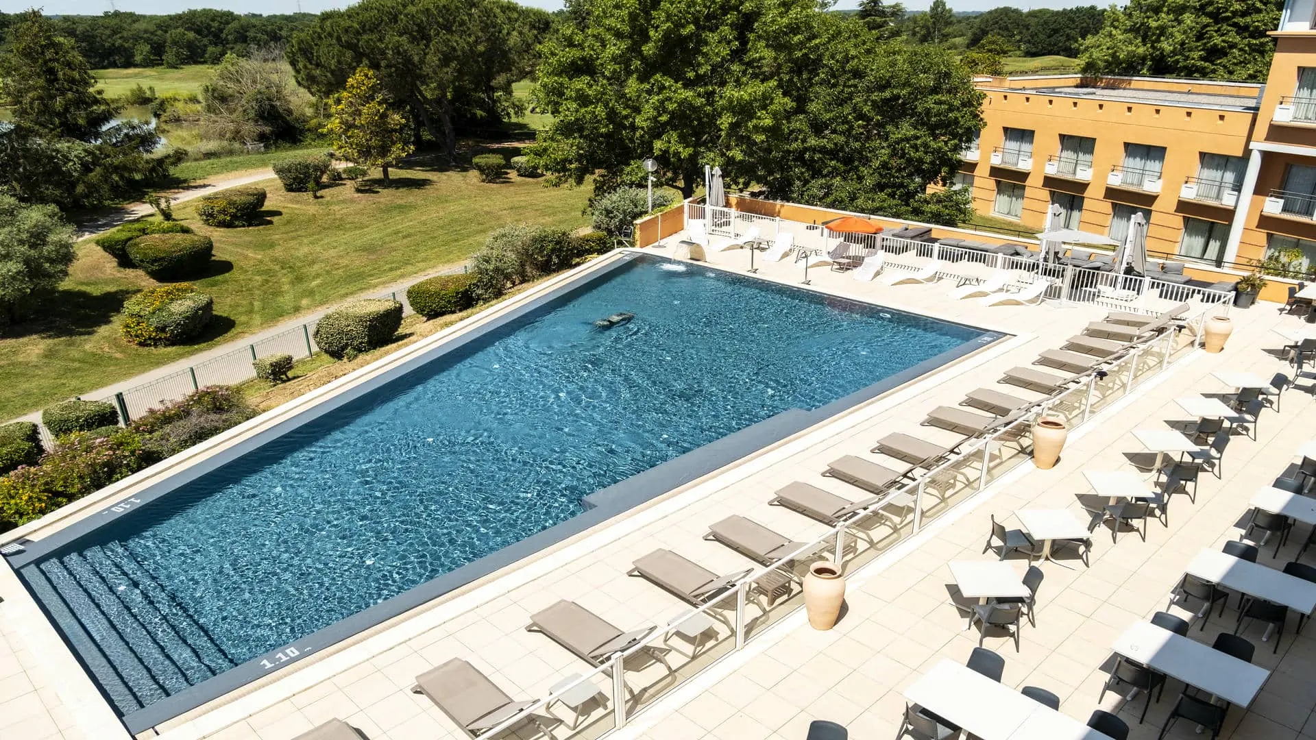 Grande piscine avec vue sur le golf, équipée de buses et d’un bec d’eau pour se détendre, bordée par la grande terrasse du restaurant séminaire.