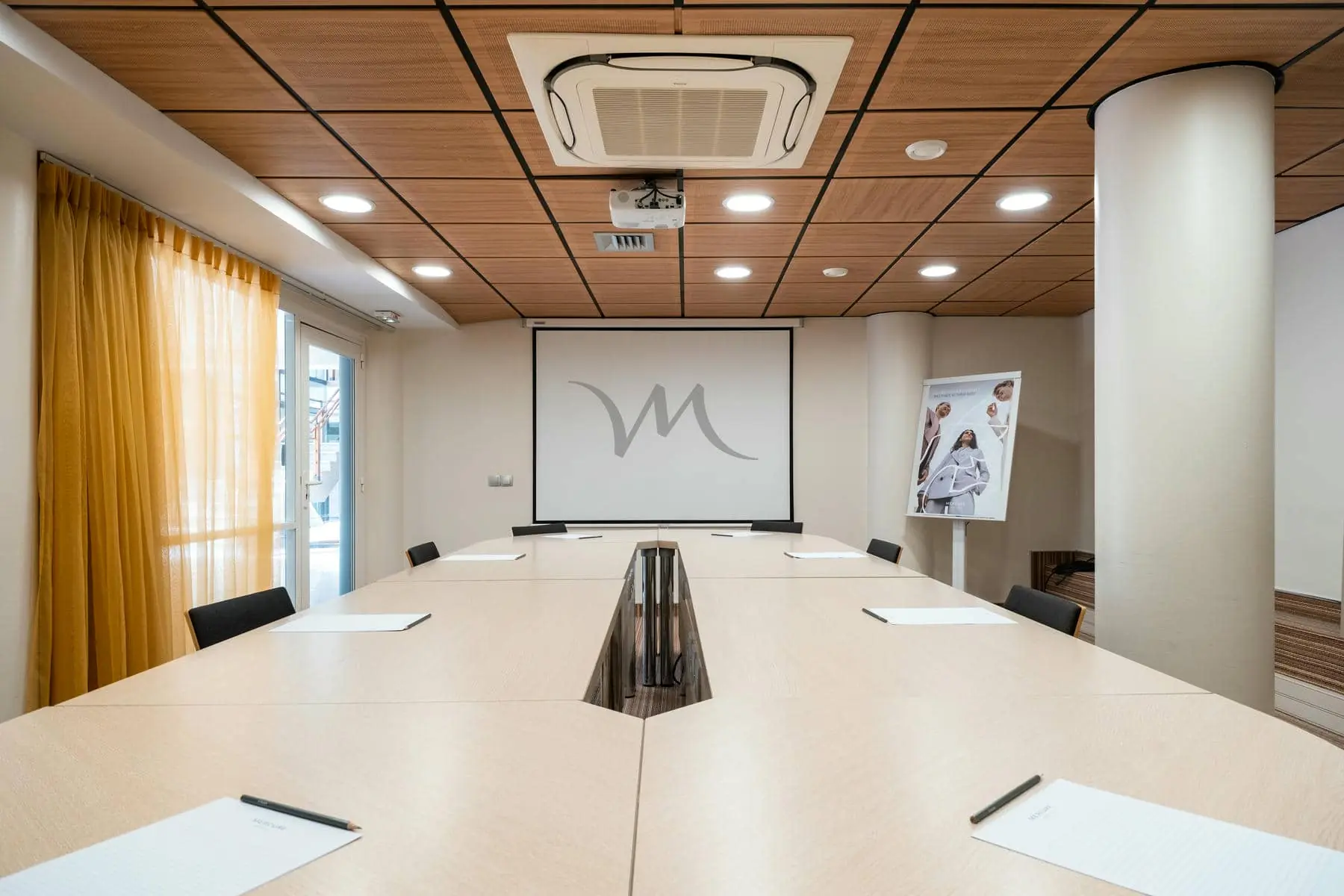une salle de conférence avec un écran de projection sur lequel figure la lettre m