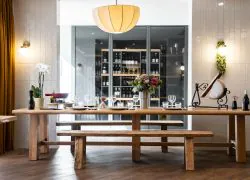 A wooden communal dining table set for raclette and fondue, with a view of the restaurant’s wine cellar, ideal for seminars and group dining.