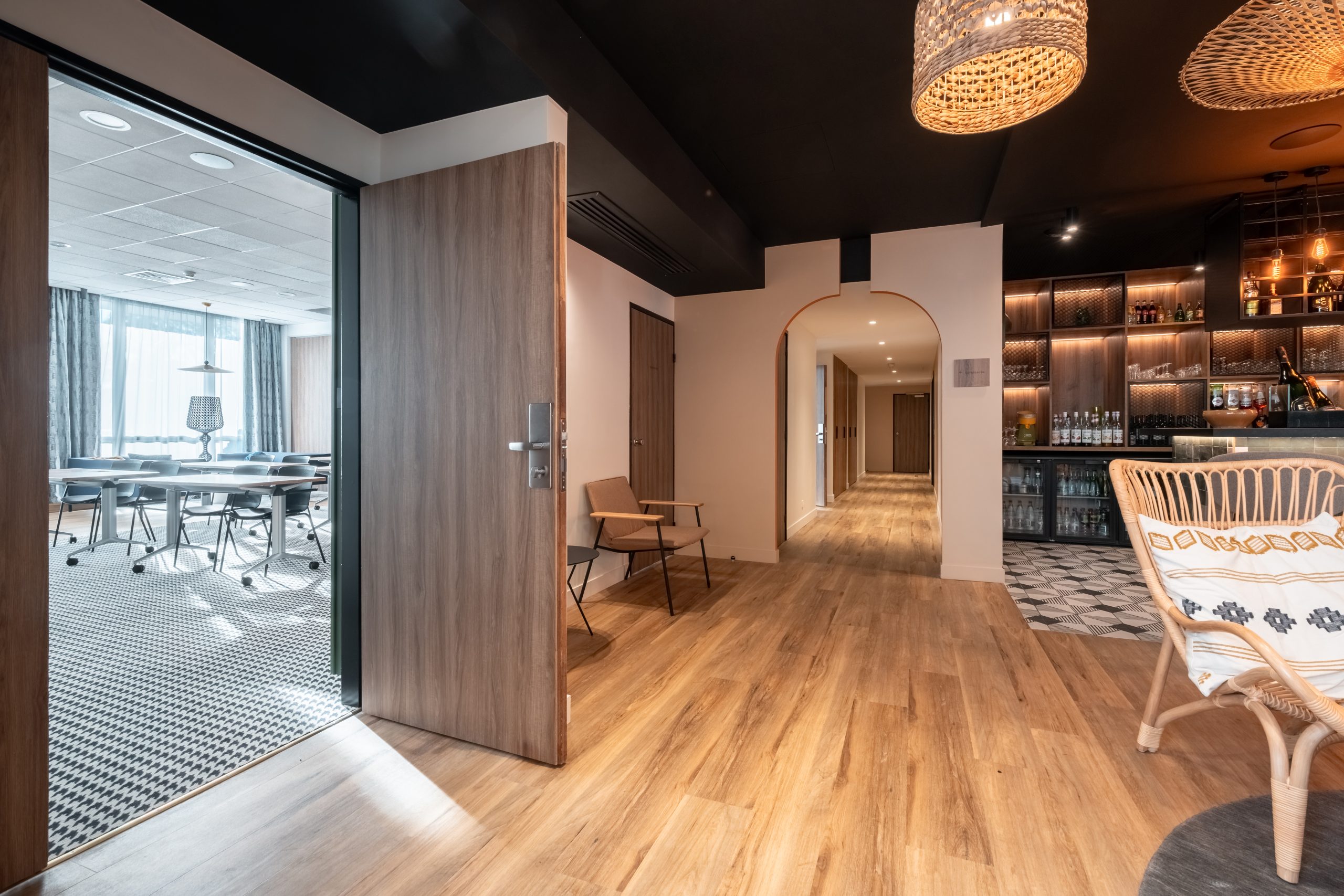en::Open seminar room door with contemporary black-and-white carpet, leading to the Novotel Chartres lobby bar with wood and natural materials. fr::Porte ouverte d’une salle de séminaire à la moquette noire et blanche contemporaine, donnant sur le lobby bar en bois et matières naturelles du Novotel Chartres.