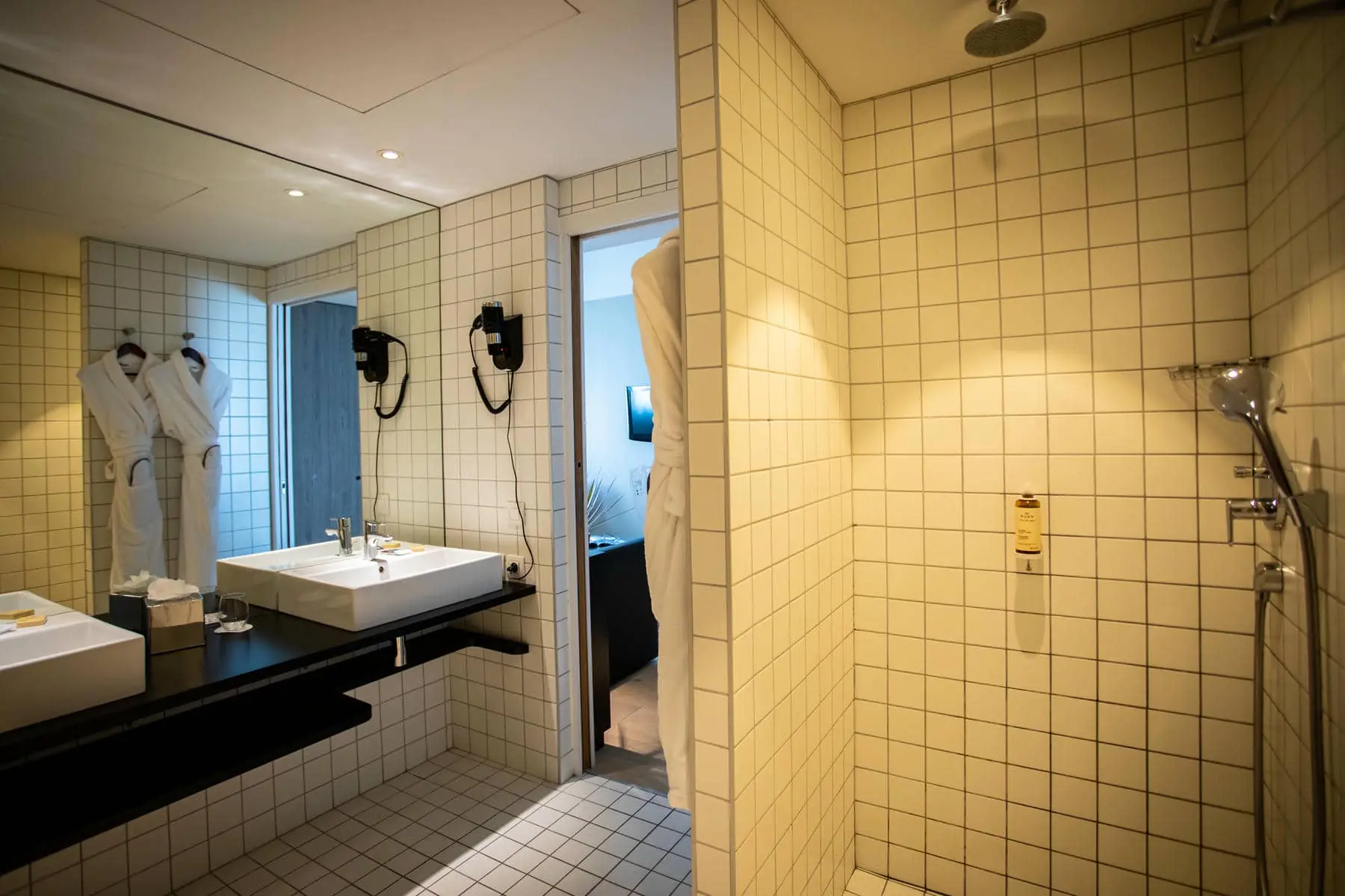 une salle de bains avec des carreaux blancs, un lavabo et une douche