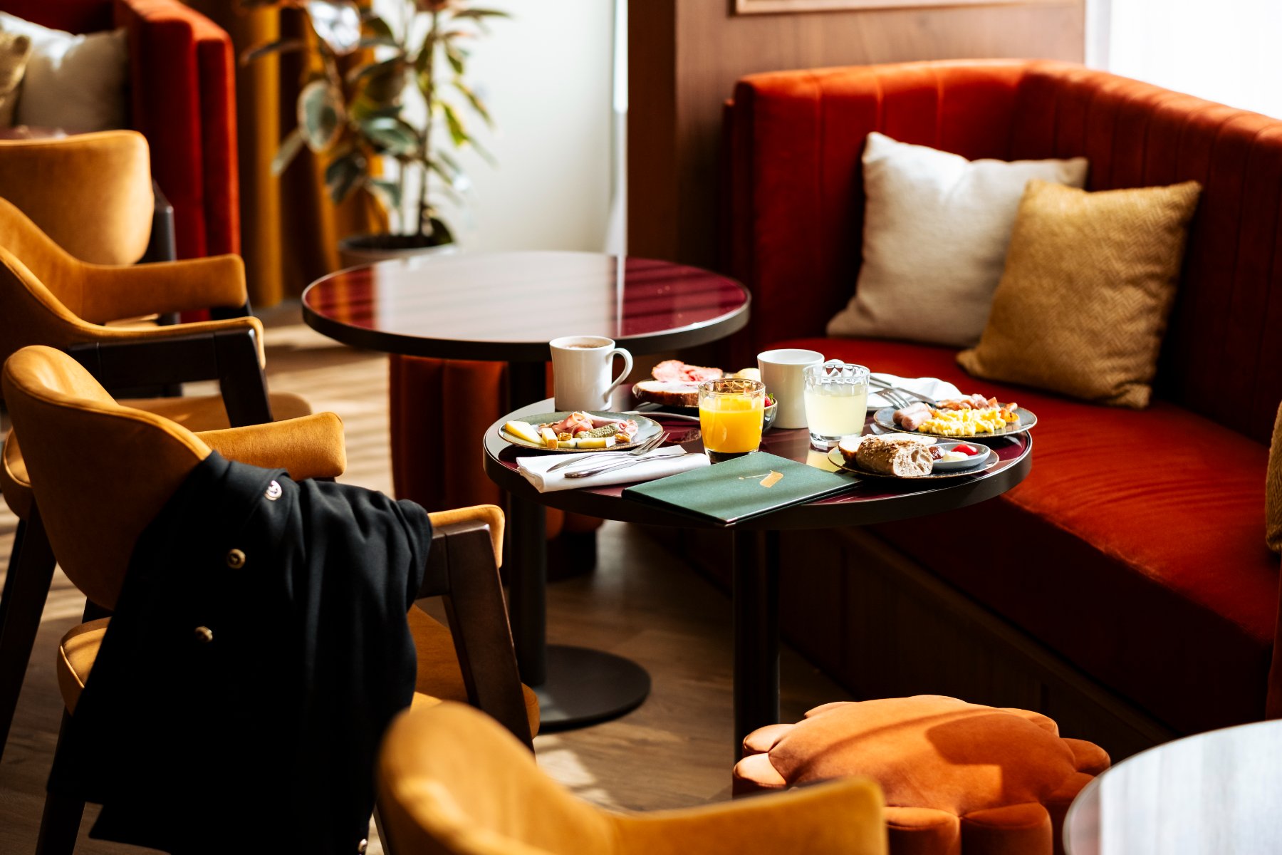 un salon raffiné avec canapé et chaises en velours, dont une avec veste de costume, table basse présentant une offre de petit-déjeuner