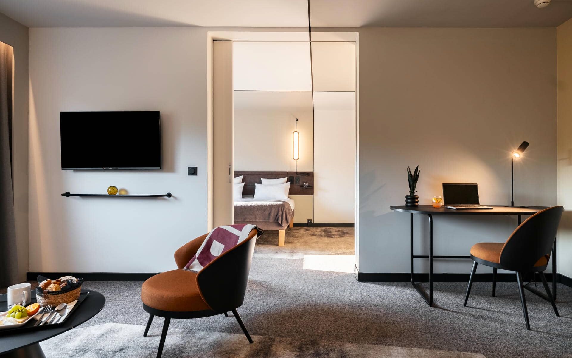 a hotel room with a desk and chairs and a flat screen tv