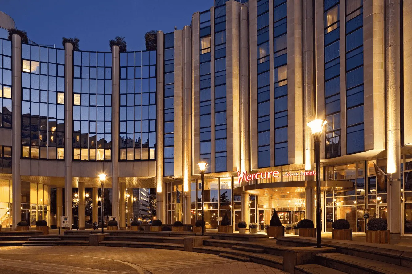 en::Large landmark building in the Boulogne-Billancourt – La Défense area, featuring the Mercure Hotels sign, night view with illuminated façade. fr::Grand bâtiment emblématique du secteur Boulogne-Billancourt – La Défense, avec enseigne Mercure Hotels, vue de nuit et façade éclairée.