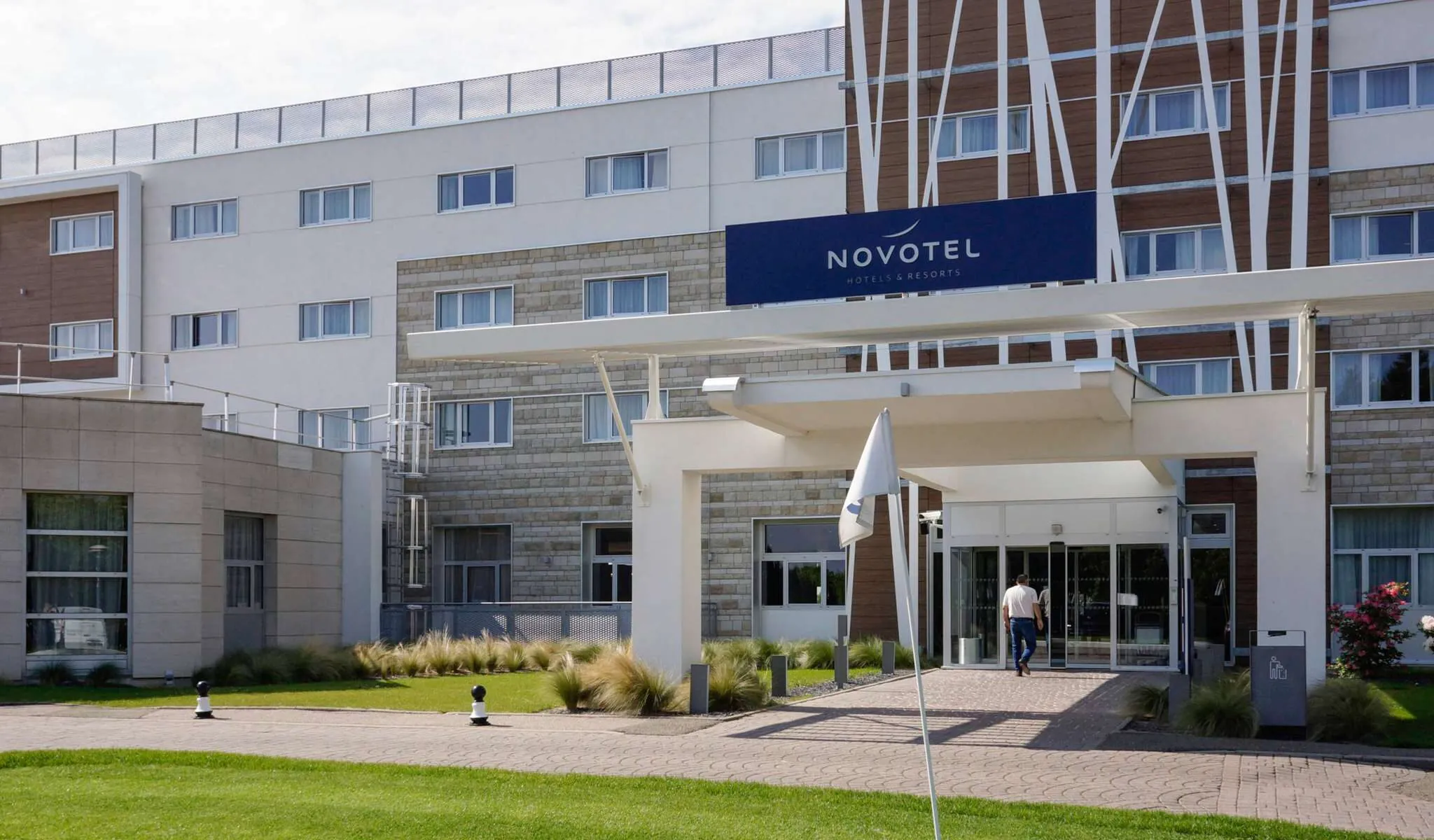 Entrée du bâtiment avec un client vu de dos en train d’entrer, face à une pelouse verte et un drapeau de golf.