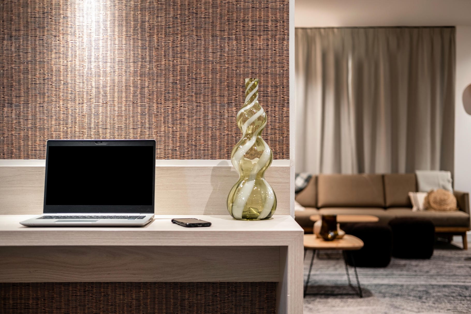 un ordinateur portable est posé sur un bureau à côté d'un téléphone et d'un vase