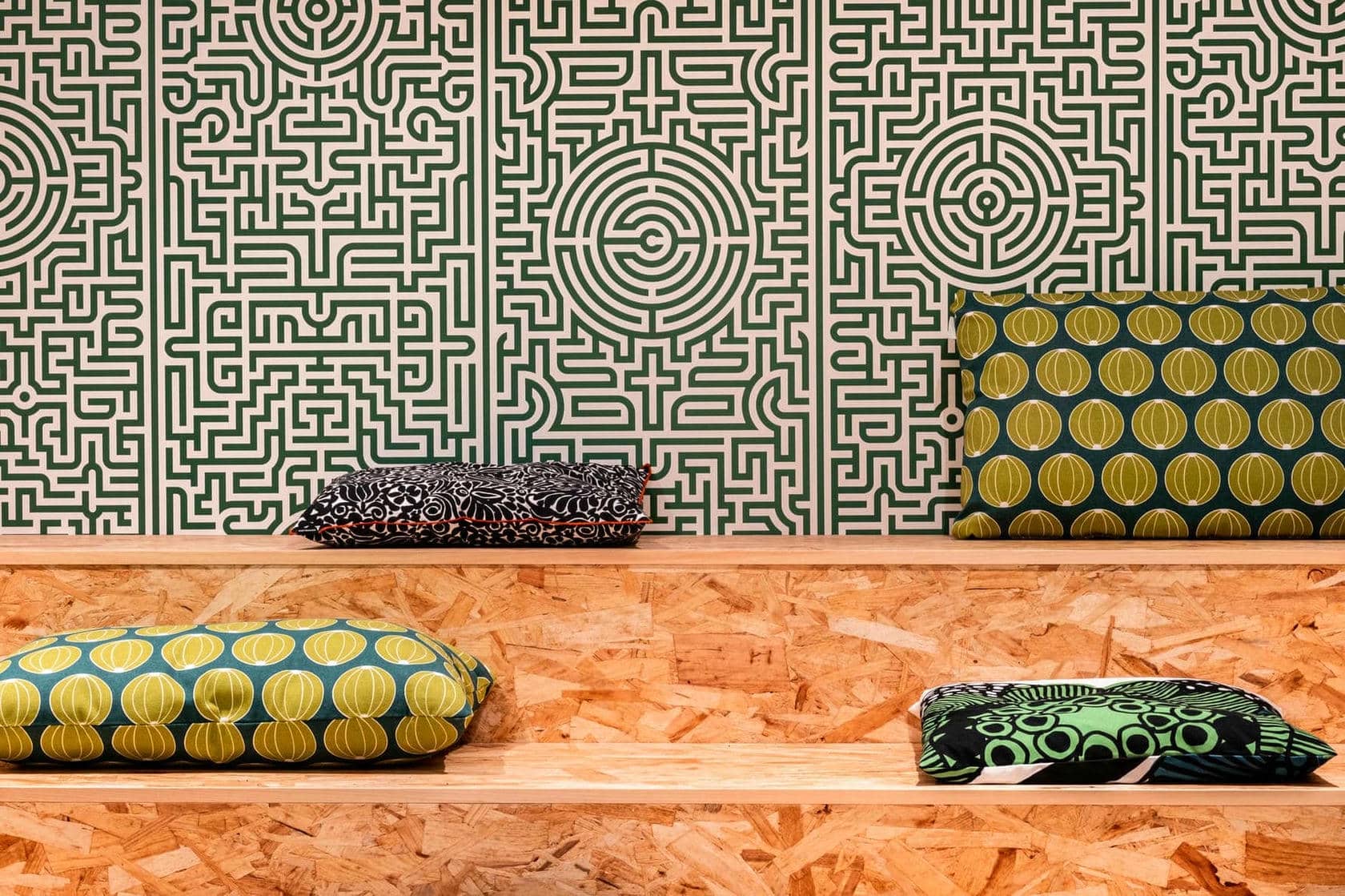 trois coussins sont posés sur une étagère en bois devant un mur à motif de labyrinthe