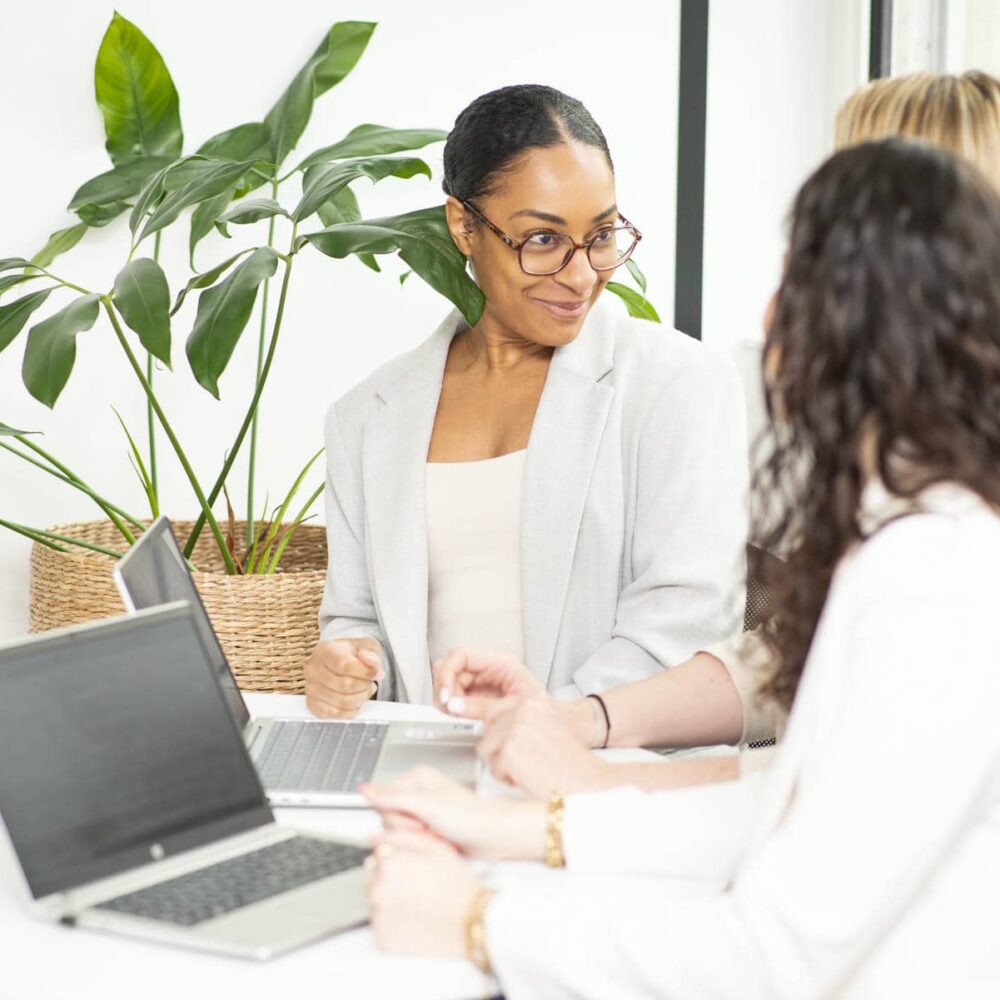 three women are sitting around a table with laptops