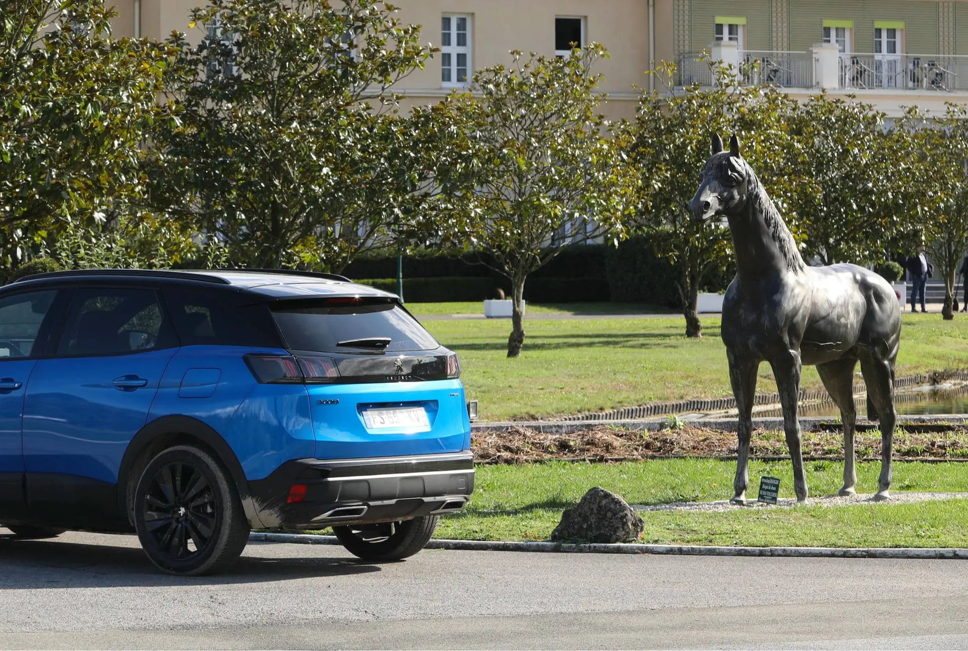 une voiture bleue est garée devant la statue d'un cheval