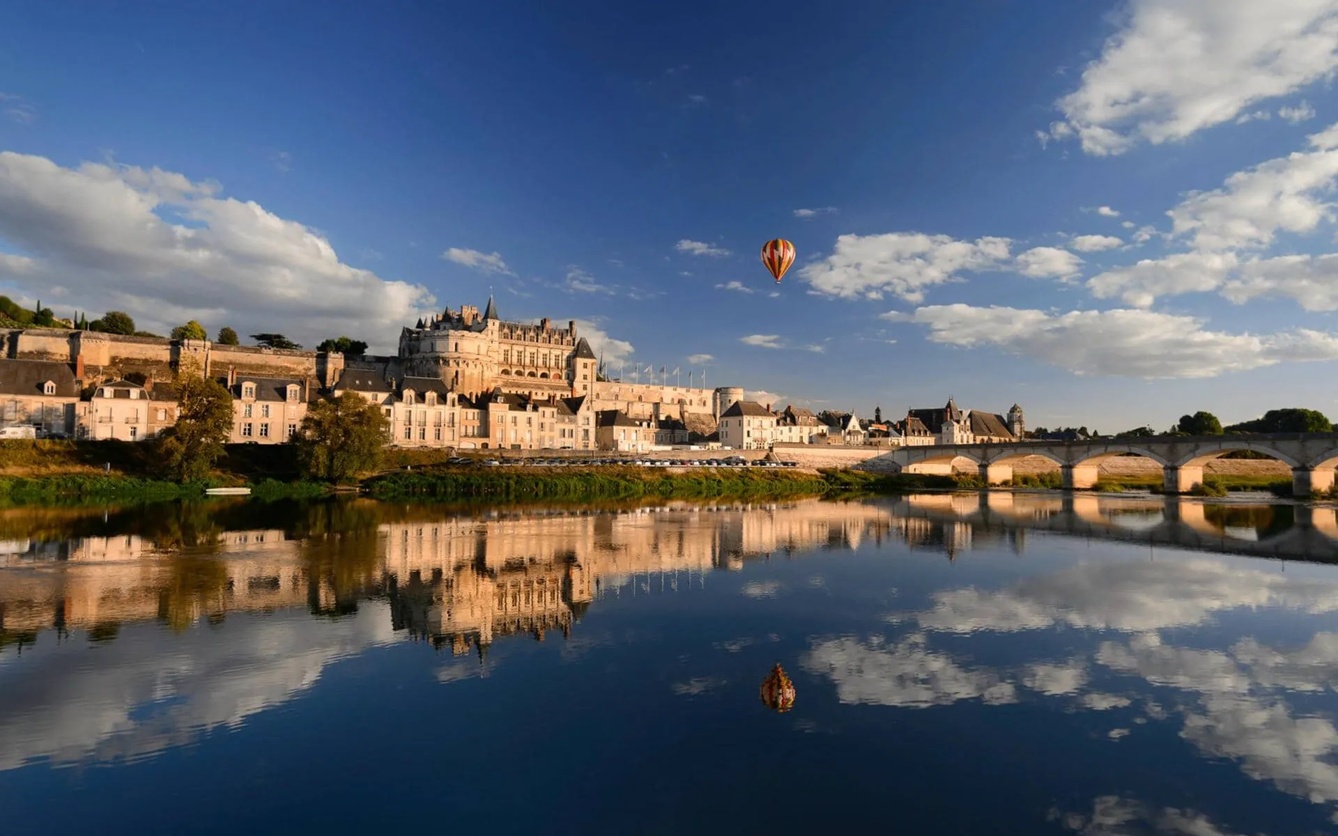 deux montgolfières survolent une rivière avec un château en arrière-plan