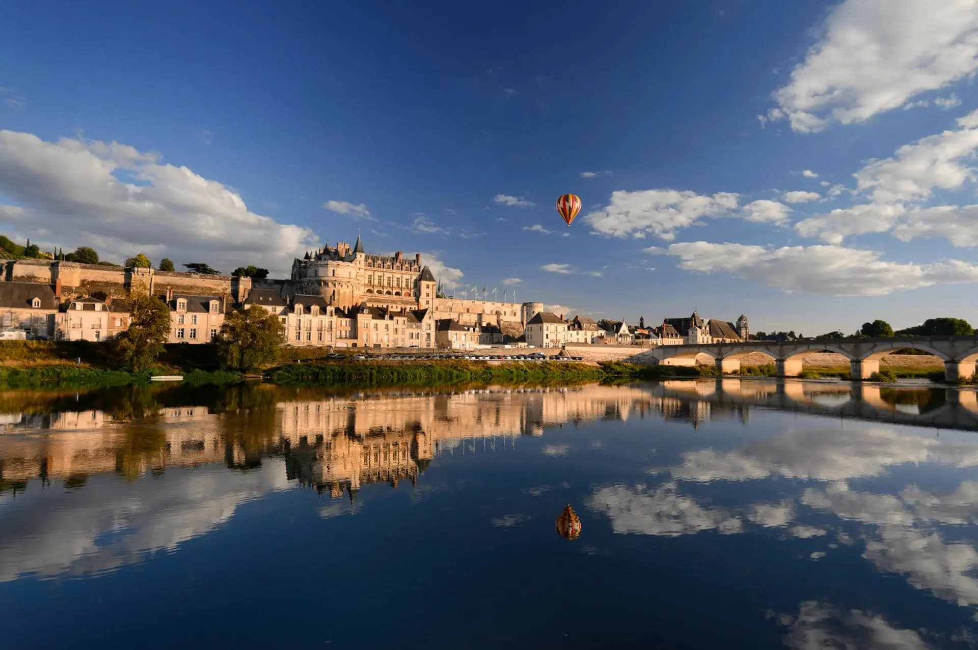 two hot air balloons are flying over a river with a castle in the background