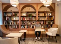 en::a person working in the library and cinema-lounge area, surrounded by books, with the forest visible across the street fr::une personne en train de travailler dans l’espace bibliothèque et ciné-lounge, entourée de livres, avec la forêt de l’autre côté de la route