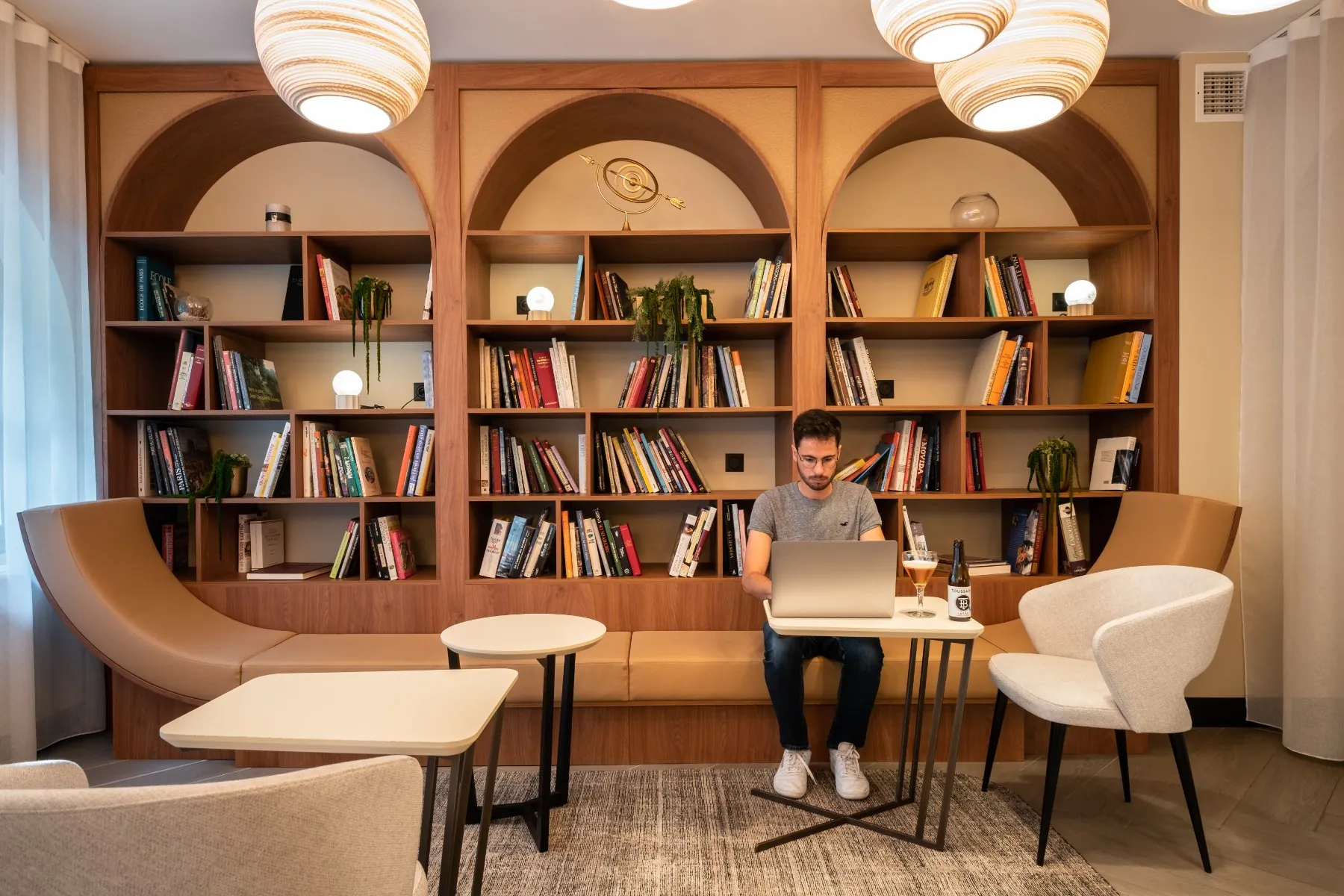 en::a person working in the library and cinema-lounge area, surrounded by books, with the forest visible across the street fr::une personne en train de travailler dans l’espace bibliothèque et ciné-lounge, entourée de livres, avec la forêt de l’autre côté de la route