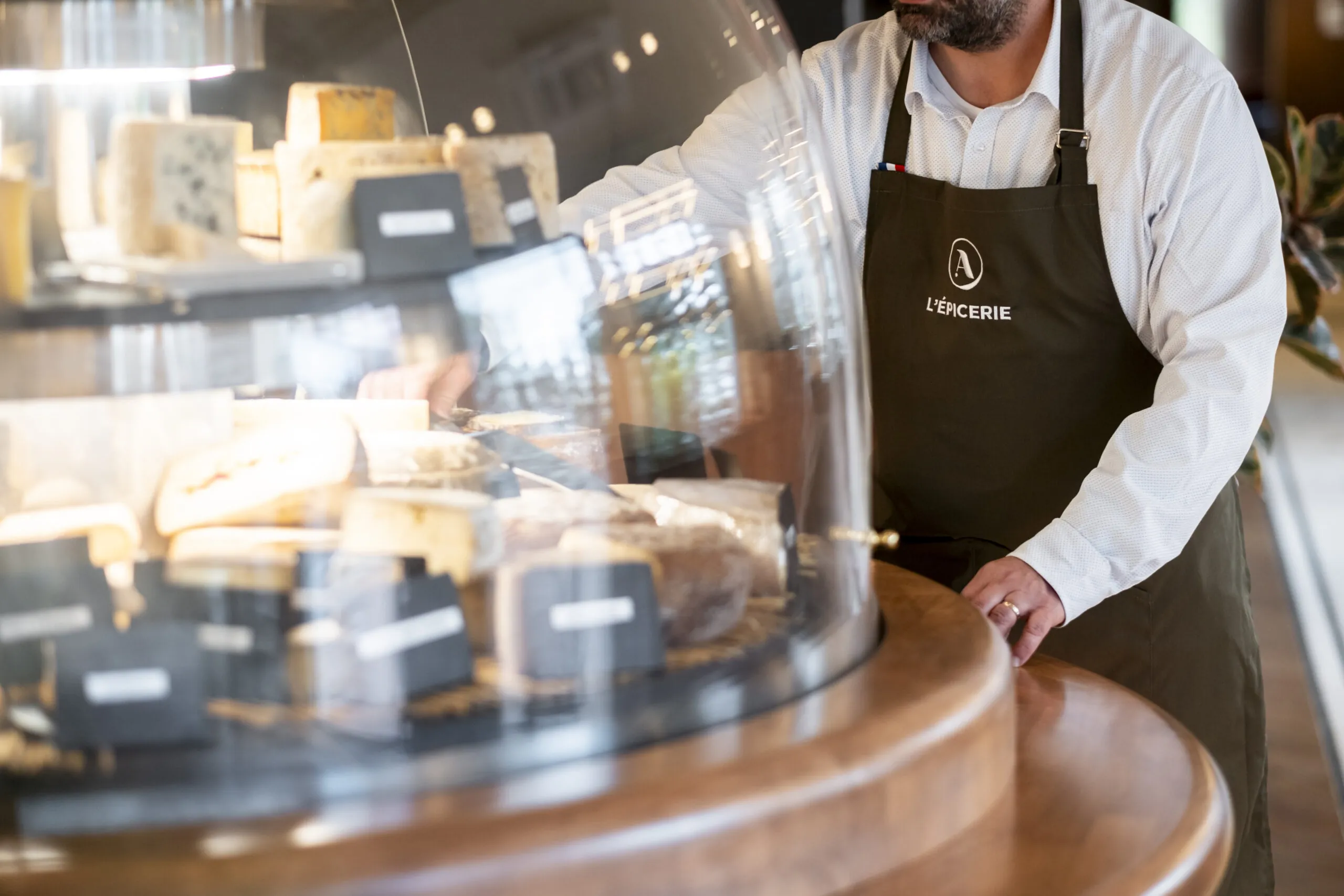 a variety of cheeses are displayed under a glass dome, with the Master Cheesemonger present