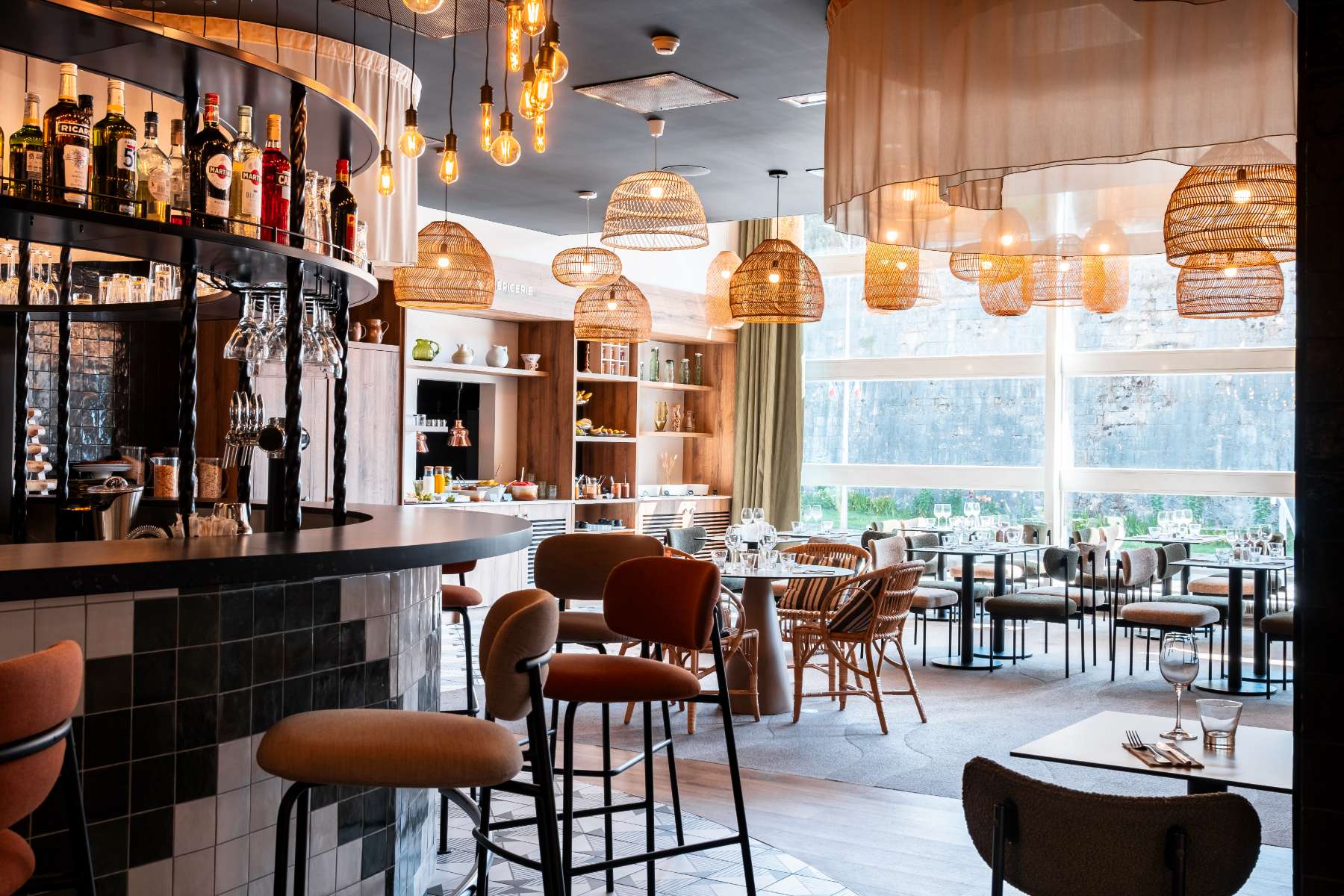 view of the restaurant dining room from the bar on the left, with sheer curtains, ceiling lights, set tables along the bay windows and a buffet unit