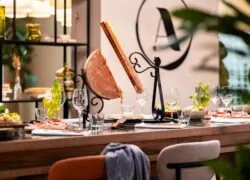 close-up of a wooden high table set for a traditional raclette, with potatoes, cured meats and the A l’Epicerie restaurant sign in the background