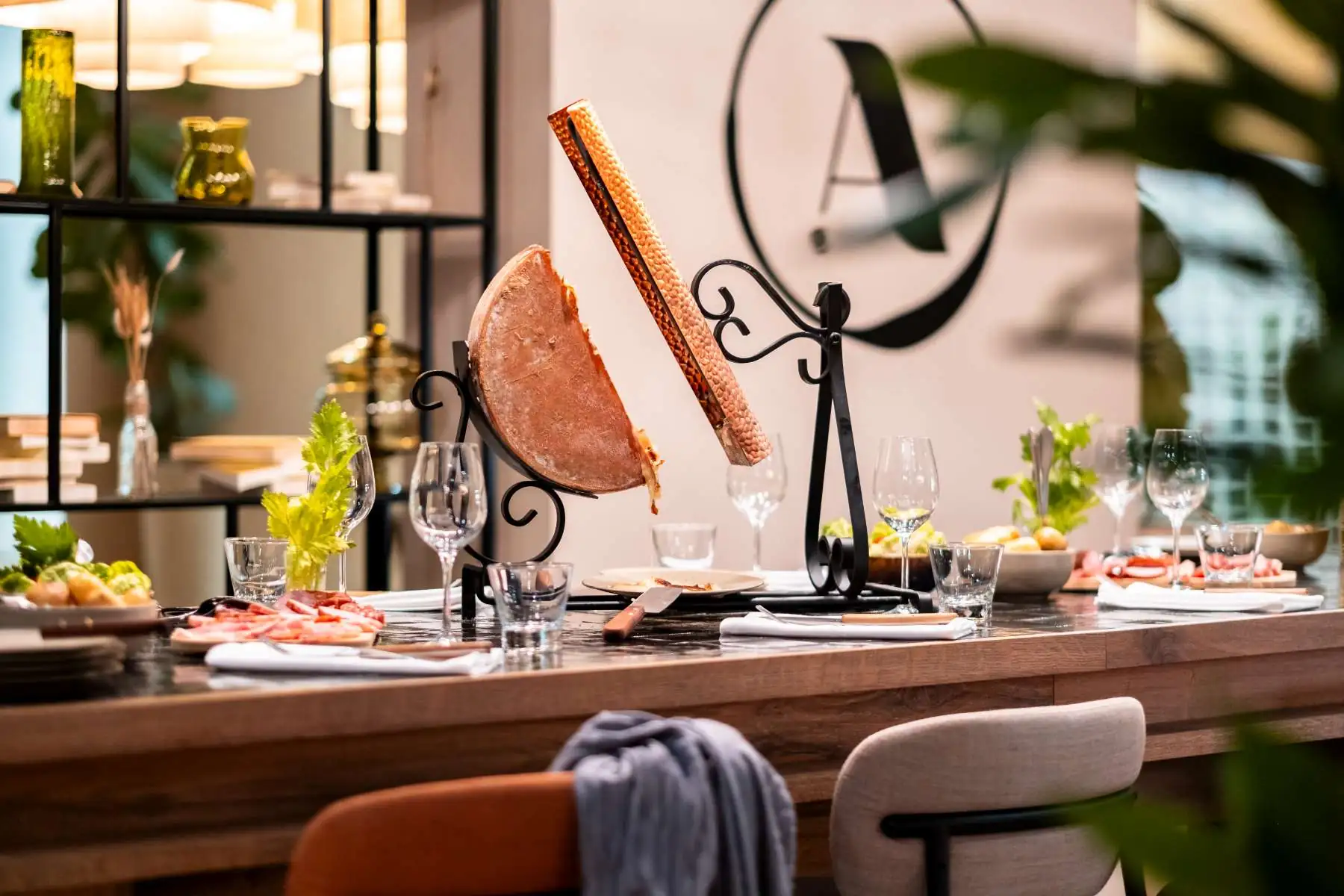 close-up of a wooden high table set for a traditional raclette, with potatoes, cured meats and the A l’Epicerie restaurant sign in the background