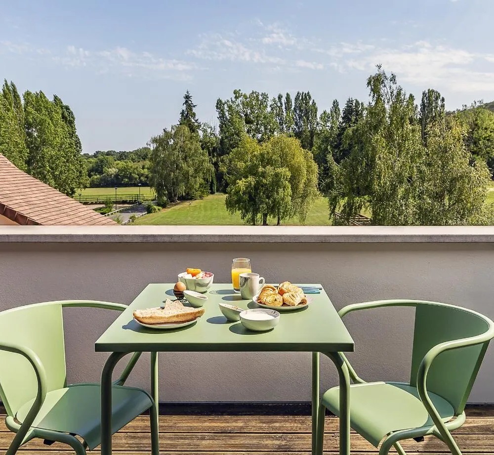 en::breakfast table set in green tones with two chairs on a private balcony, overlooking the tree-filled park and horses in the distance fr::table de petit déjeuner verte dressée sur le balcon d’une chambre, avec deux chaises, vue sur le parc arboré et des chevaux au loin