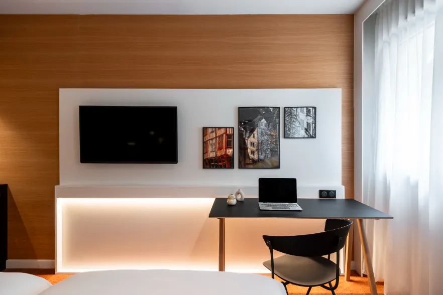 room with a close-up on a metal-and-wood desk, warm indirect lighting, a wall-mounted television, and framed photographs of Normandy