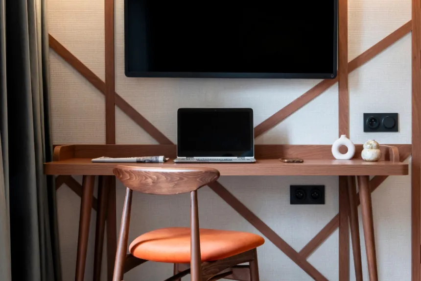privilege room with a close-up on the wooden desk, wooden seating with an orange chair, wall-mounted television, and a Norman half-timbered pattern reproduced on the background wall