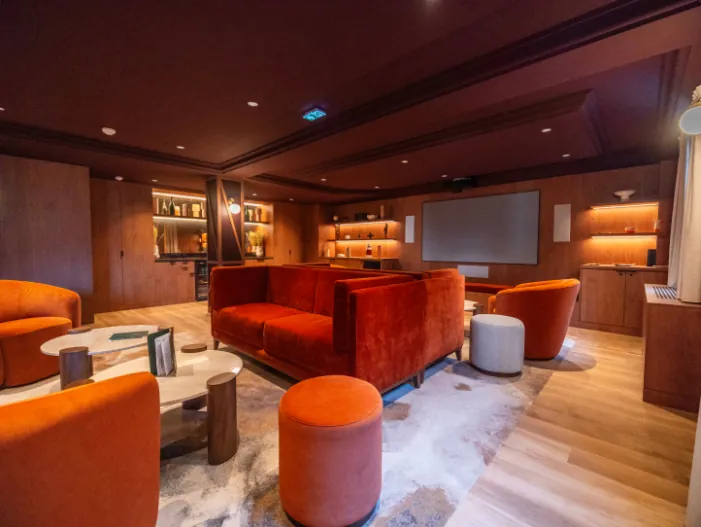 a cinema lounge area with a screen, sofas, armchairs, tables, a bookcase