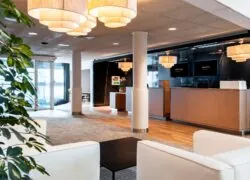 hotel lobby with a children’s play area, wooden reception desk, white leather armchairs and lights fixture made of three rings