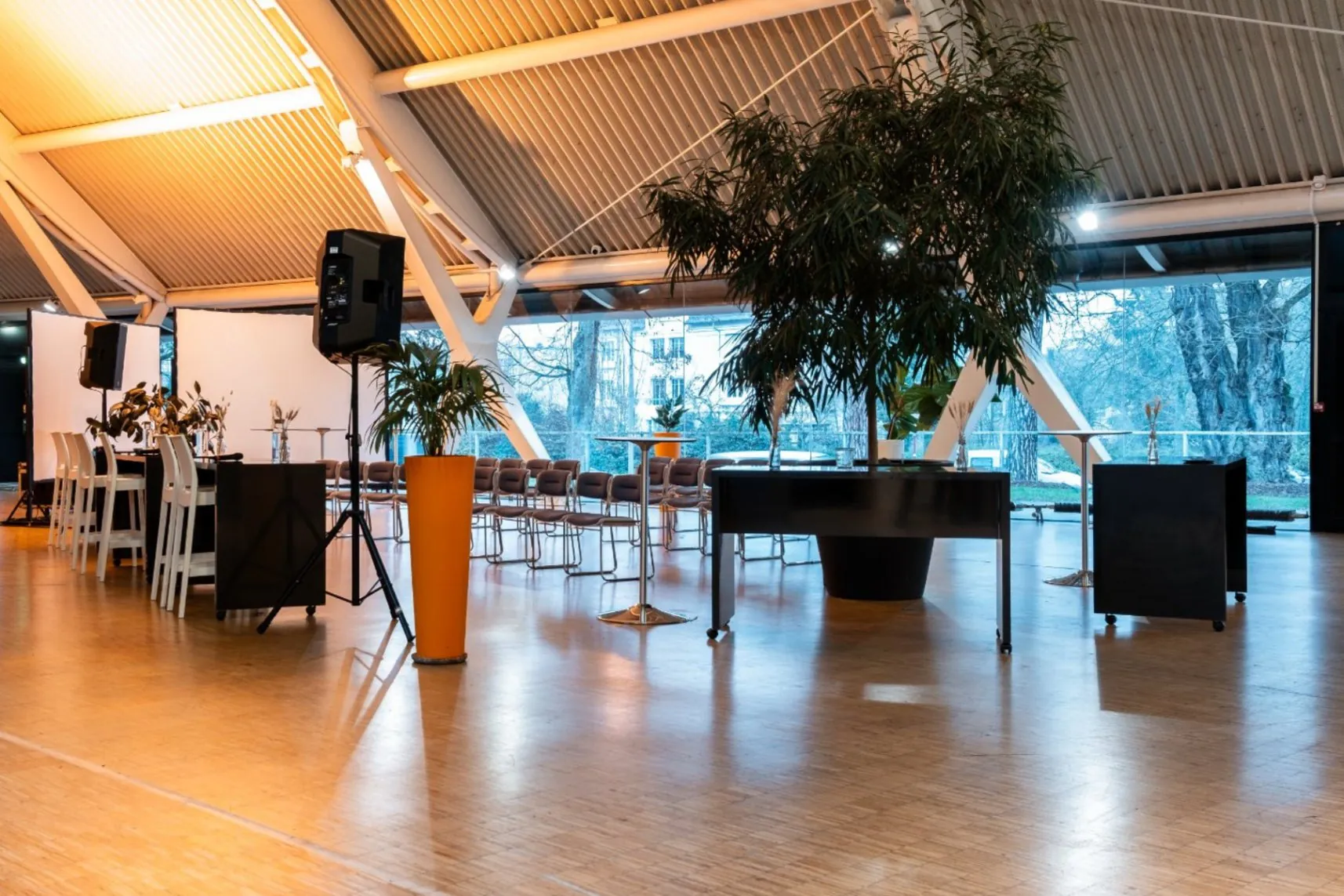meeting room overlooking the city and surrounding greenery, featuring low and high chairs, a few high tables, two large screens and plants