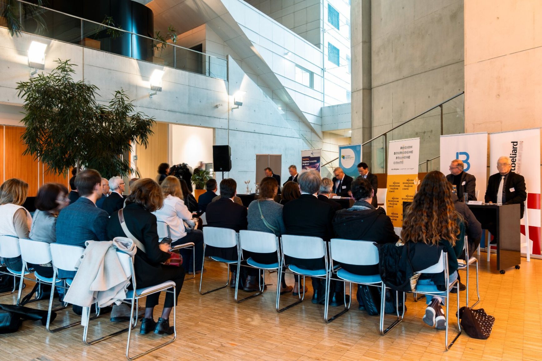 high-angle view of a meeting room, with speakers presenting their project to three rows of attendees