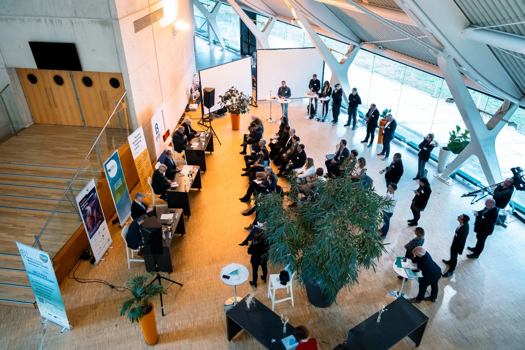 high-angle view of a meeting room, with speakers presenting their project to several rows of attendees