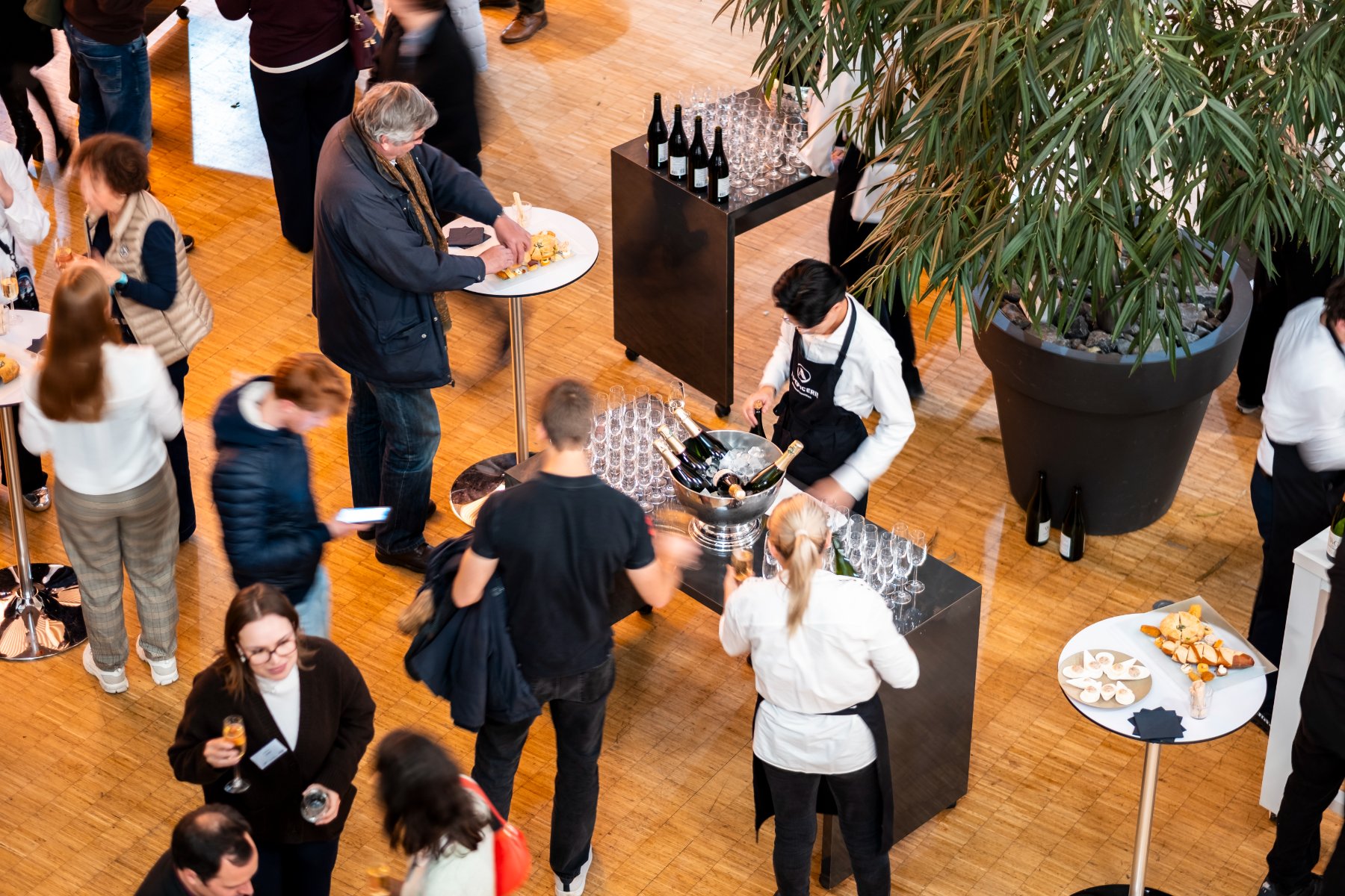 high-angle view of a meeting room set up for a cocktail reception, with business guests, hotel staff, and tables displaying food and drinks