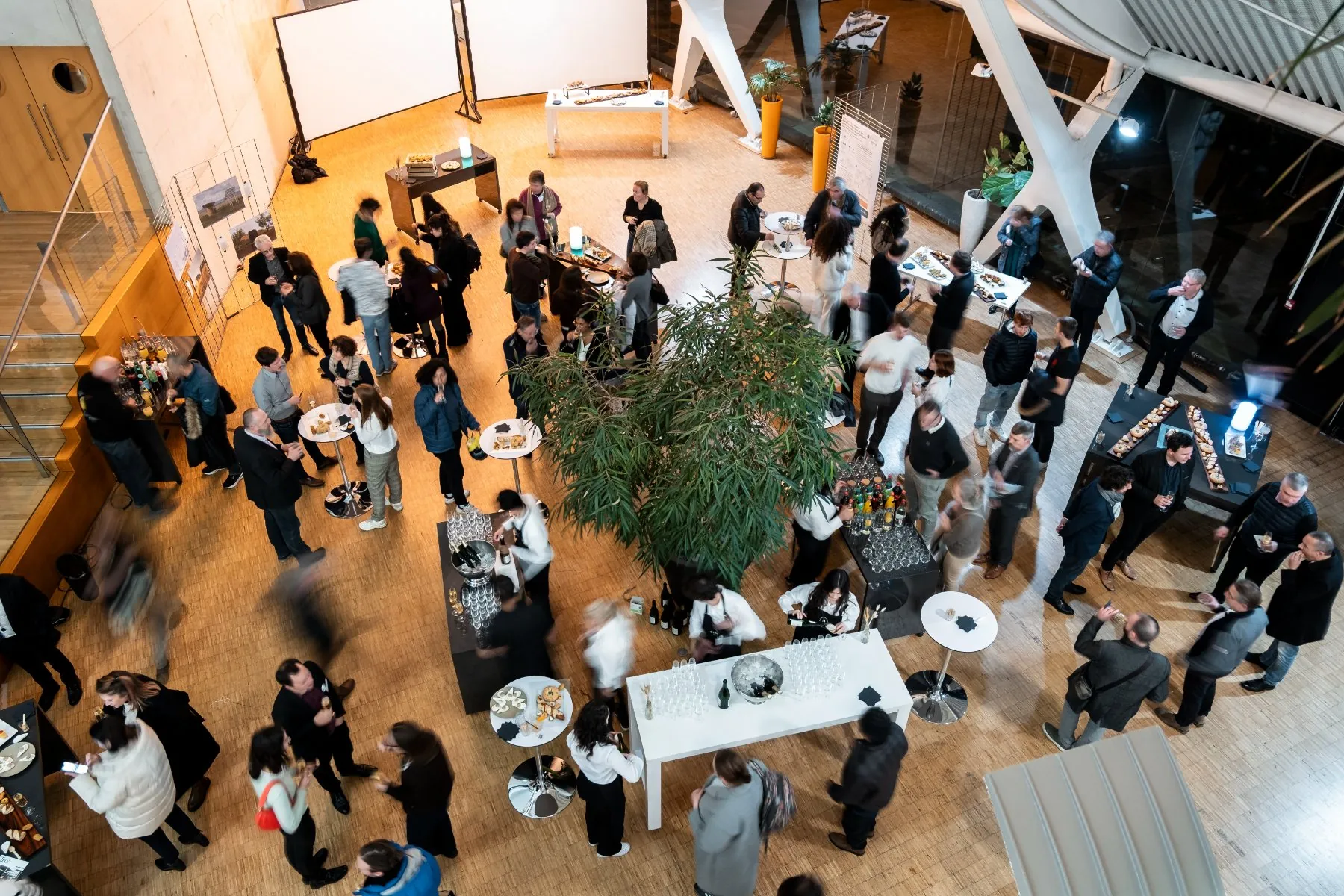 high-angle view of a meeting room set up for a cocktail reception, with business guests, hotel staff, and tables displaying food and drinks