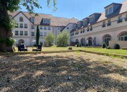 a view of the hotel façade facing the inner garden, with L-shaped buildings in the background, the terrace and a pétanque court in the foreground