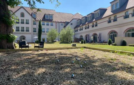 vue de la façade de l’hôtel côté jardin intérieur, avec en arrière-plan des bâtiments formant un L, la terrasse et, au premier plan, le boulodrome