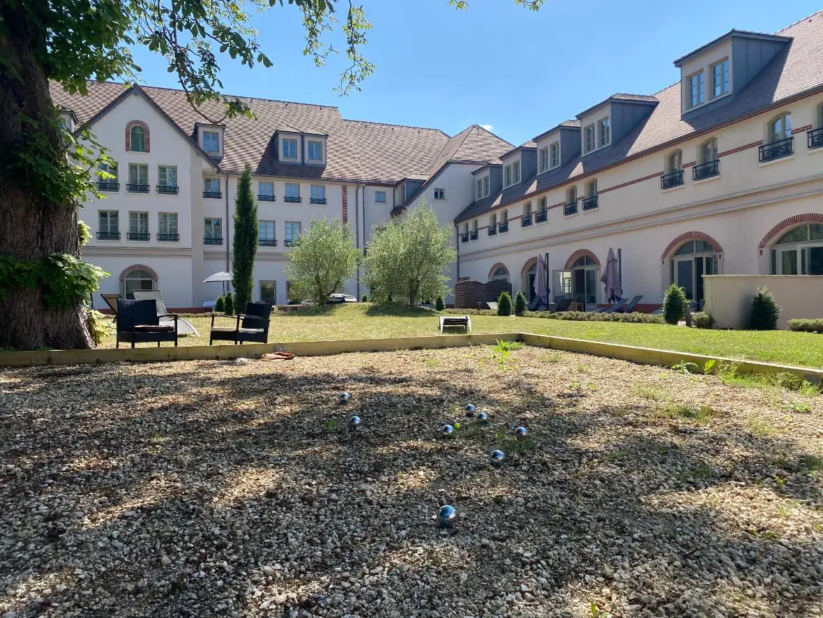 vue de la façade de l’hôtel côté jardin intérieur, avec en arrière-plan des bâtiments formant un L, la terrasse et, au premier plan, le boulodrome