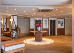 hall d’accueil avec table centrale fleurie, ascenseurs en face et bibliothèque sur la gauche