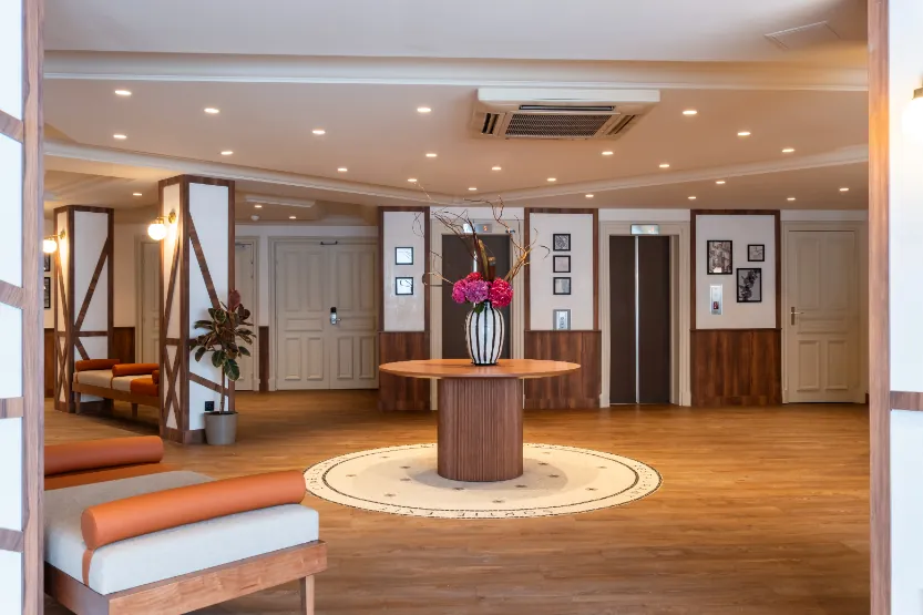 hotel lobby with a central table and floral arrangement, elevators ahead, and a library on the left