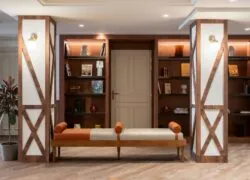 grand meuble bibliothèque en deux parties, encadré de colonnes habillées de bois, avec un banc esprit boudoir et des livres disposés de part et d’autre