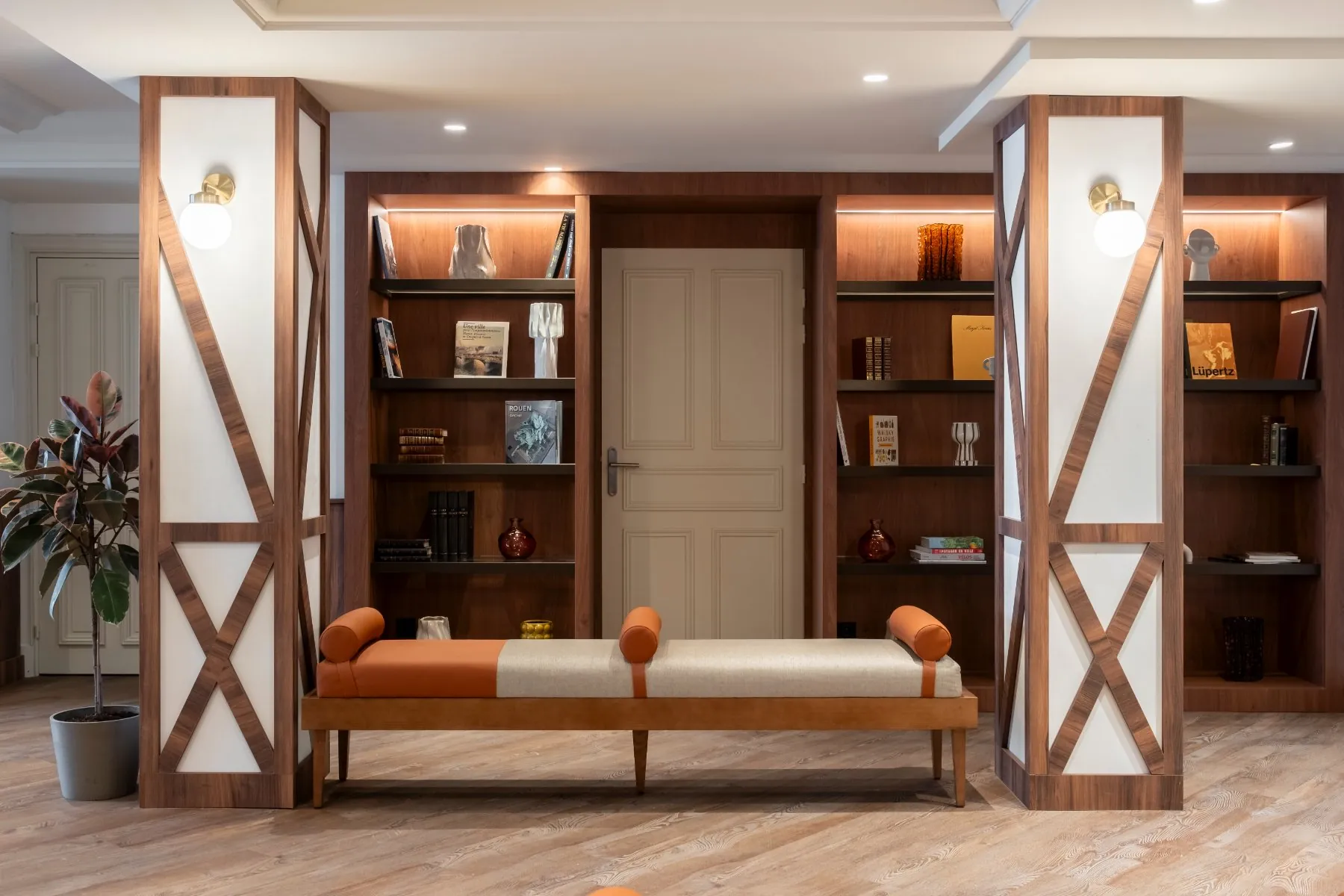library lounge area with a large wooden bookcase framed by two columns, a boudoir-style bench, and books displayed on either side