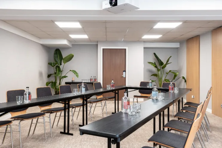 rows of chairs arranged in a U-shape meeting room, with a ceiling-mounted projector, viewed from the window toward the door