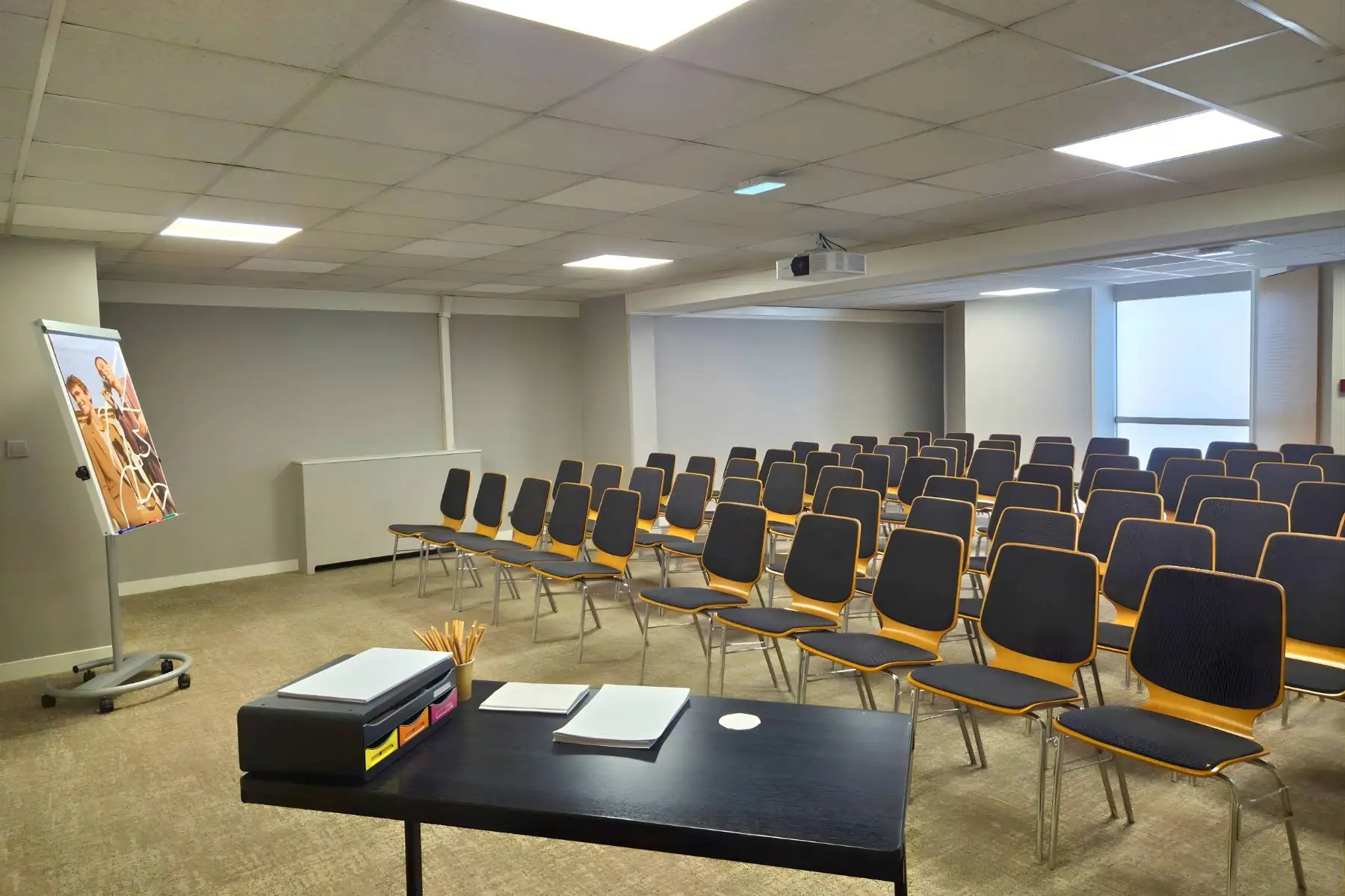 meeting room with rows of chairs arranged in theater style facing a screen, with a desk shown at an angle