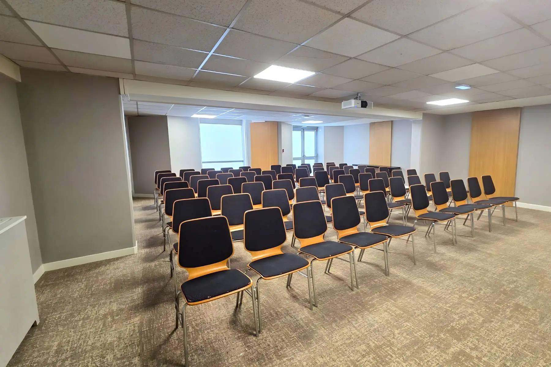 meeting room with rows of chairs arranged in theater style facing a screen suggested by the ceiling-mounted projector