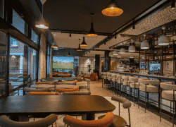 en::Set tables along the restaurant’s floor-to-ceiling windows overlooking the golf course and the pool, a central bar with seating on both sides, a wide counter for buffet or cocktail receptions facing the pool, and a lounge area with a screen at the entrance. fr::Tables dressées le long des baies vitrées du restaurant, avec vue sur le golf et la piscine, bar central avec fauteuils de chaque côté, large comptoir pour buffet ou cocktail et espace lounge avec écran à l’entrée