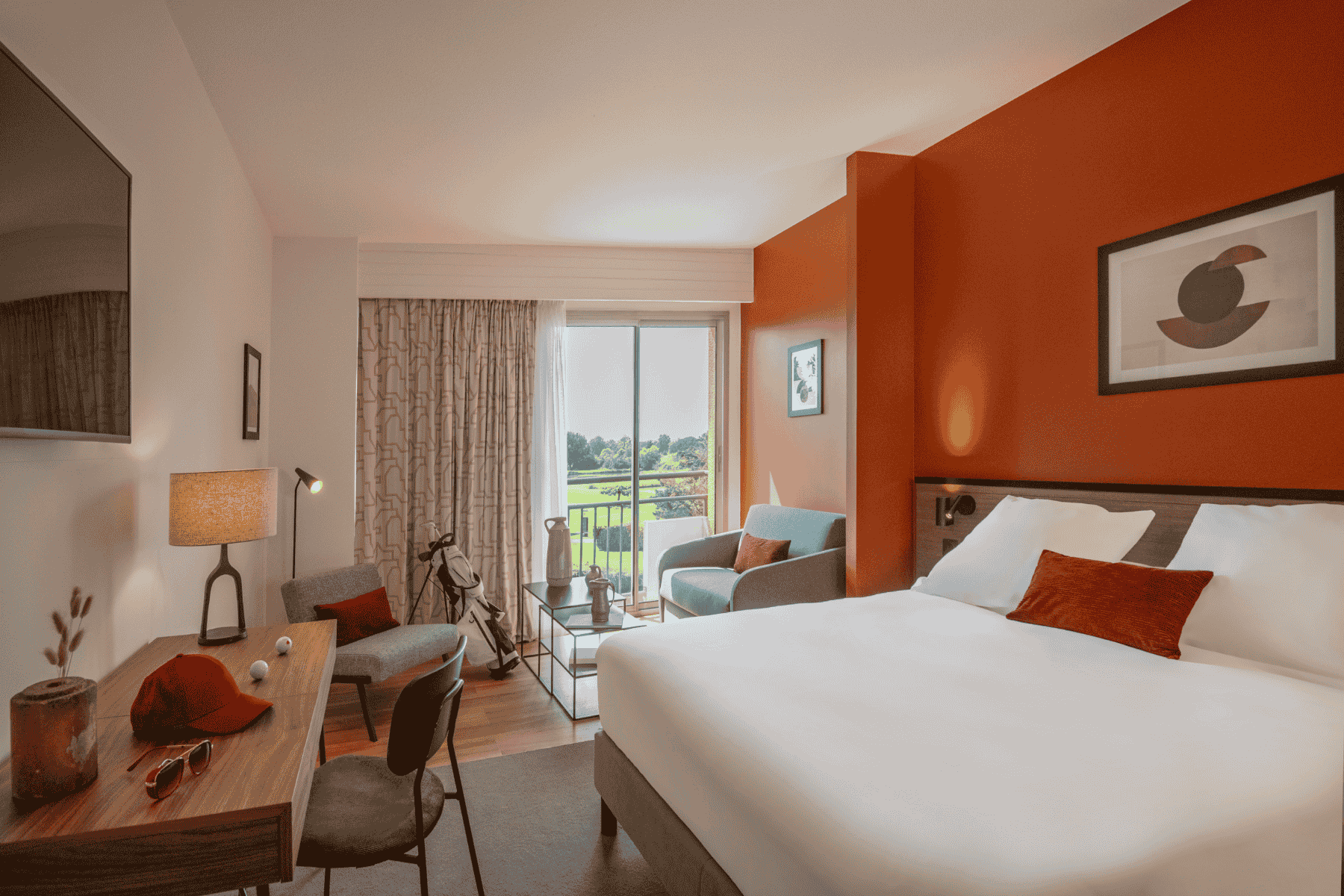 en::Superior room with golf course views through large floor-to-ceiling windows, partially shaded by beige geometric curtains and sheer drapes, featuring a double bed, desk, and a seating area with an armchair, coffee table, and golf bag. fr::Chambre supérieure avec vue sur le golf à travers de larges baies vitrées partiellement occultées par des rideaux et voilages beiges à motifs géométriques, lit double, bureau, et coin salon avec fauteuil, table basse et sac de golf.