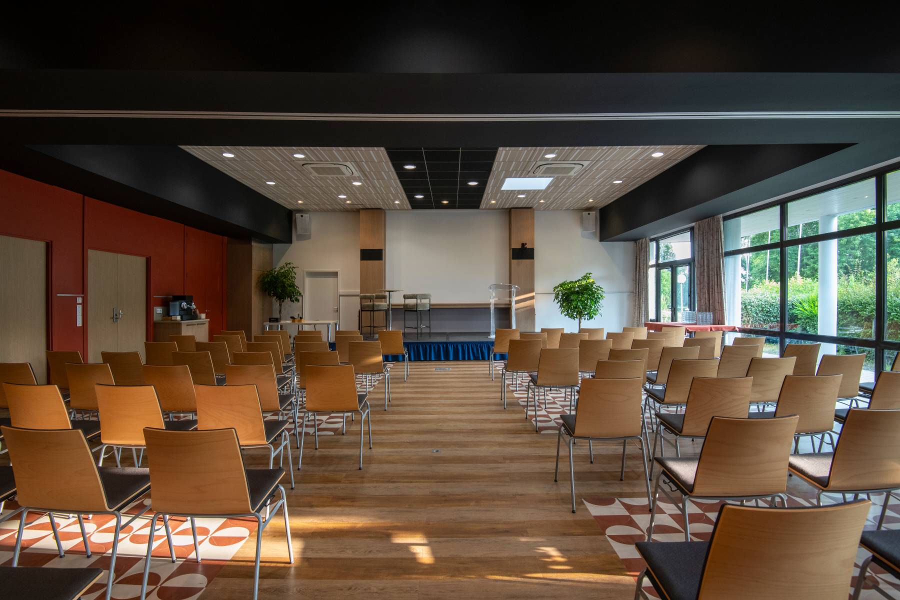 Large meeting room in wood and red tones with bay windows overlooking the golf course, stage at the back of the room and chairs arranged in theatre layout