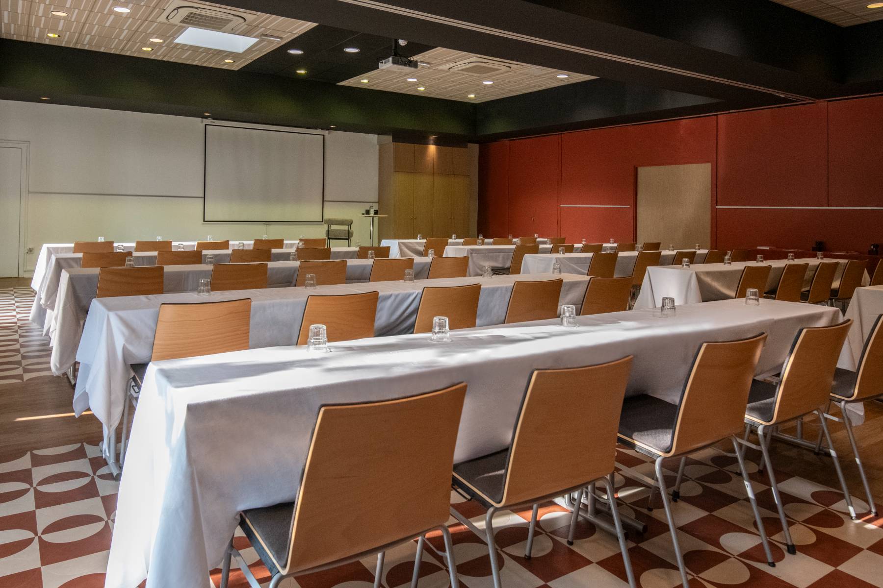 Large tables with chairs are arranged facing a screen in classroom layout