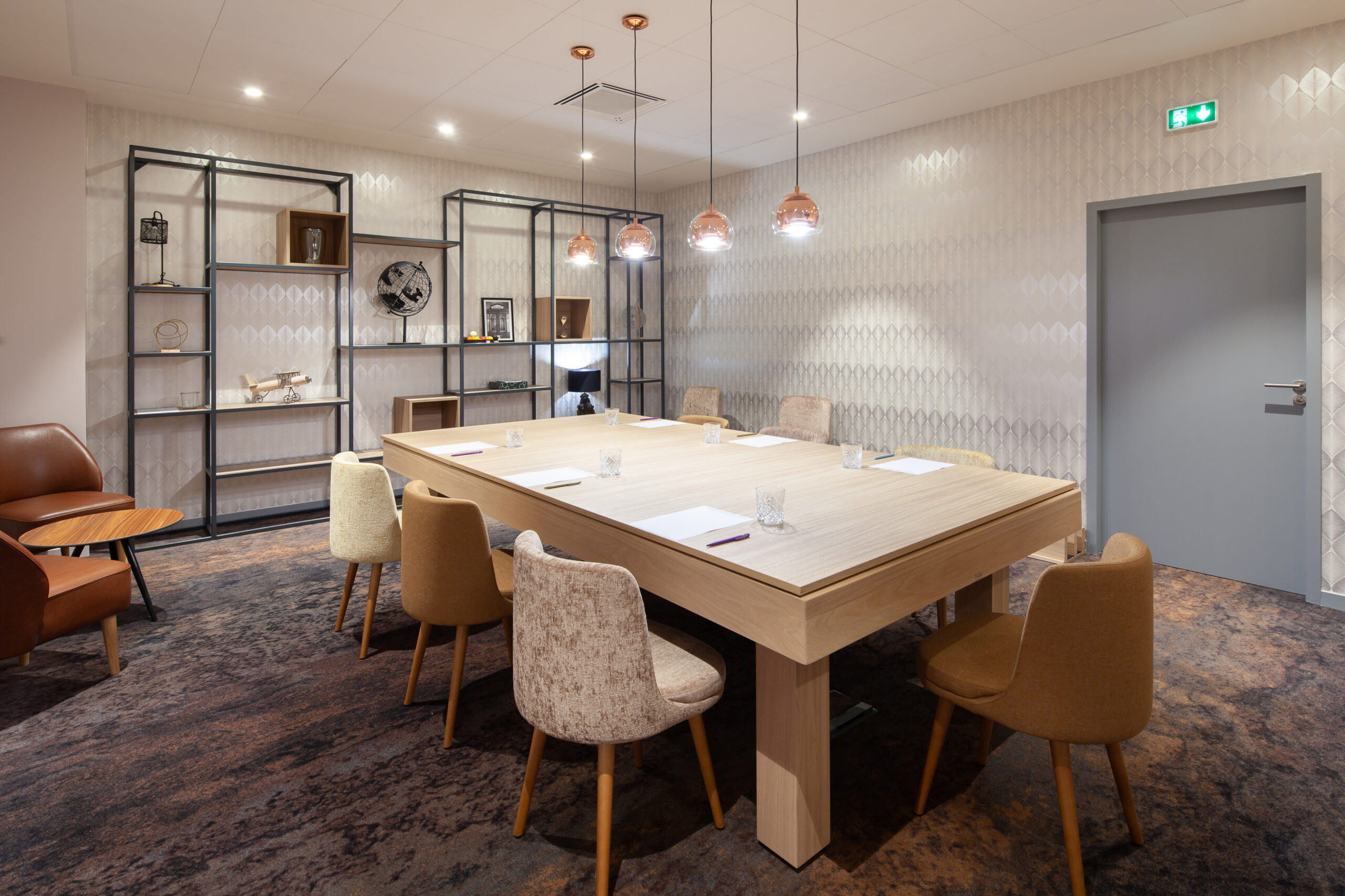 en::Large wooden table for eight with glasses, notepads and pencils, round pendant lights above, small lounge area and décor. fr::Grande table en bois pour 8 personnes avec verres, blocs-notes et crayons, luminaires ronds suspendus, coin salon et décoration.